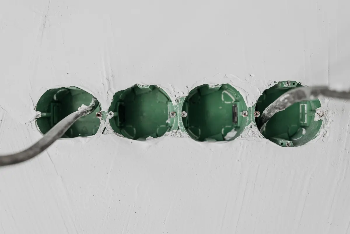 Close-up of green electrical boxes and wiring in a wall setup.